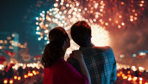 A couple watches fireworks together, illuminated by colorful lights against a night sky.