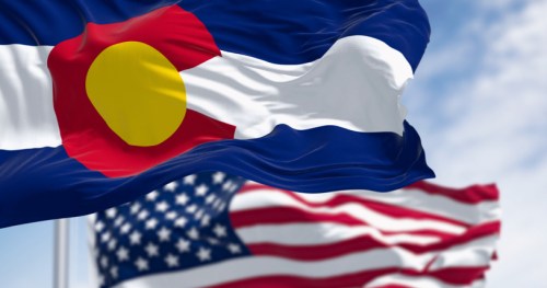 Waving flags of Colorado and the United States against a blue sky.