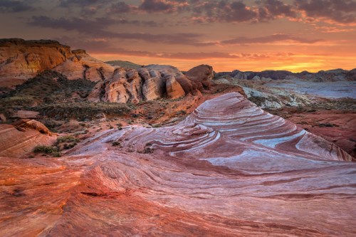 Vibrant sunset over colorful rock formations in a desert landscape, showcasing layered textures and hues.