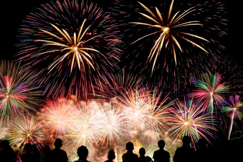 Silhouettes of people watching a vibrant fireworks display lighting up the night sky with colorful bursts.