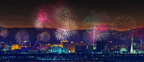 Colorful fireworks illuminate the Las Vegas skyline at night, with mountains in the background and city lights glowing.