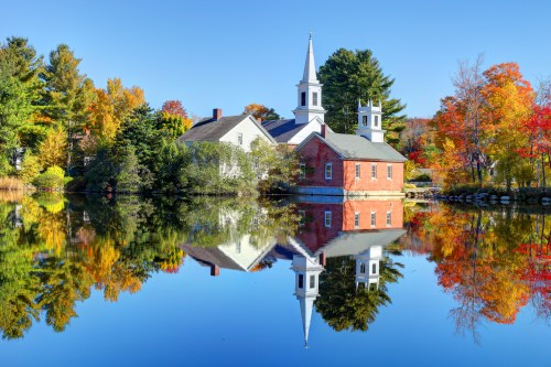 A picturesque church by a calm lake, surrounded by vibrant autumn foliage and clear blue skies.