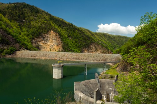 A serene landscape featuring a calm reservoir surrounded by lush green hills and a concrete dam structure.