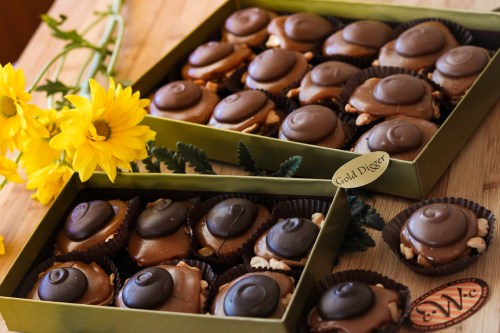 Two boxes of chocolate treats with a swirl on top, surrounded by yellow flowers on a wooden surface.