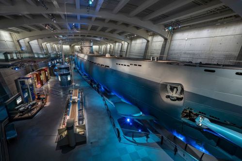 A large submarine displayed in a modern museum, surrounded by exhibits and illuminated with blue lighting.