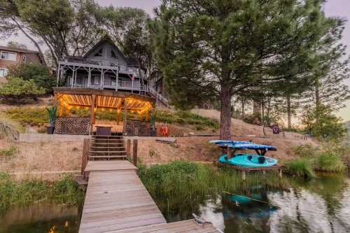 A cozy lakeside house with a deck, surrounded by trees, and kayaks hanging by the water on a serene evening.