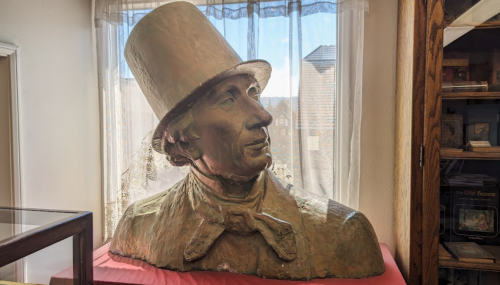 A large bust of a man wearing a tall hat, displayed indoors with natural light and a lace curtain in the background.