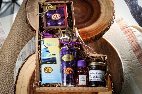 A gift box featuring huckleberry products, including chocolate, honey, and a decorative card, arranged on wooden slices.