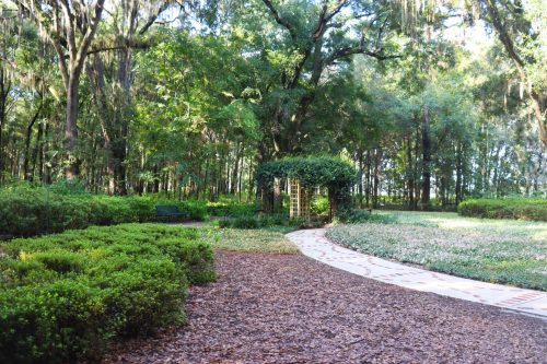 A serene garden path winding through lush greenery, with a trellis and benches nestled among the trees.