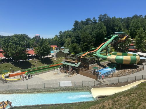 Aerial view of a water park featuring colorful slides, a lazy river, and lush green trees in the background.