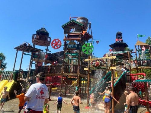 A water park with colorful slides and play structures, filled with children playing and splashing in the water.