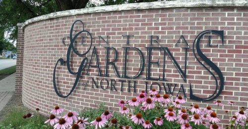 Sign for Central Gardens of North Iowa, featuring a brick wall and colorful flowers in the foreground.
