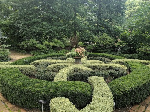 A neatly trimmed garden with a central planter surrounded by lush greenery and decorative hedges.