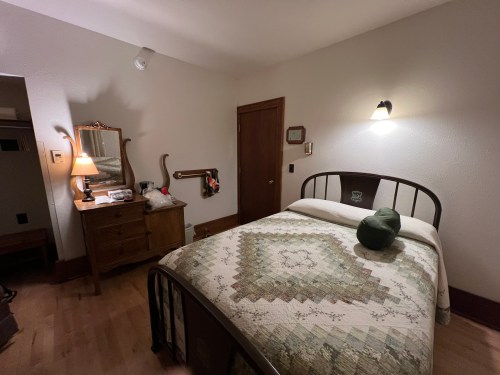 A cozy bedroom featuring a bed with a quilt, a wooden dresser, and soft lighting.