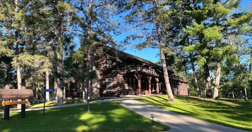 A rustic lodge surrounded by tall trees, featuring a sign for Douglas Lodge and a well-maintained lawn.