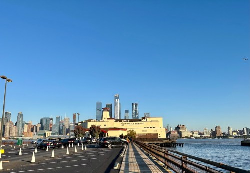 View of a waterfront with a building and city skyline under a clear blue sky.