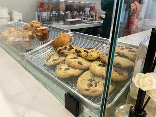A display case with freshly baked cookies and pastries, including chocolate chip cookies and croissants.