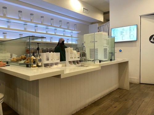 A modern café interior with a glass display counter, pastries, and a menu screen on the wall.