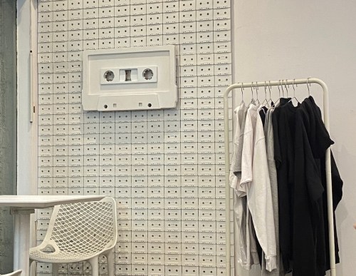 A wall decorated with cassette tapes and a large cassette design, alongside a clothing rack with black and white shirts.