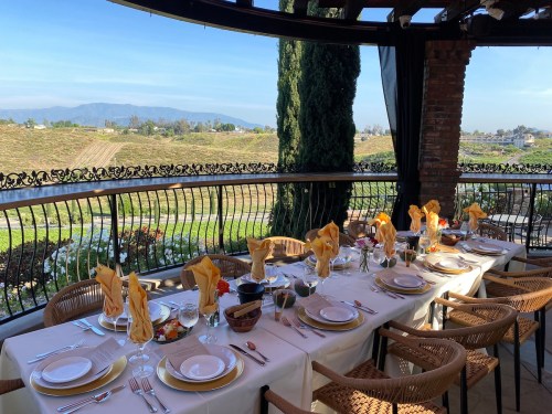 A beautifully set outdoor dining table with yellow napkins, overlooking a scenic vineyard and mountains in the background.