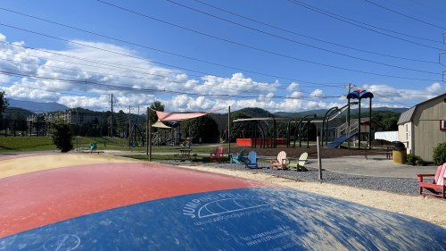 A colorful inflatable jumping pillow in a playground with mountains and blue skies in the background.