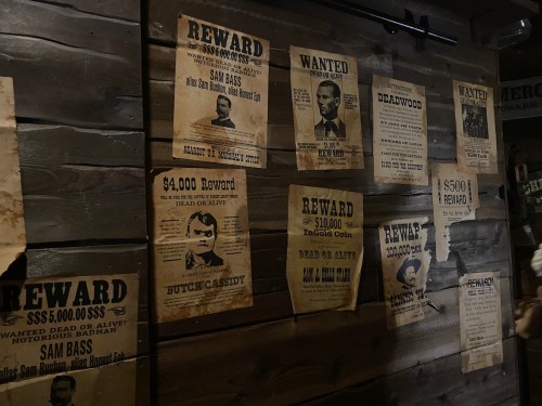A wall covered with old wanted posters, featuring rewards for outlaws like Butch Cassidy and Sam Bass.