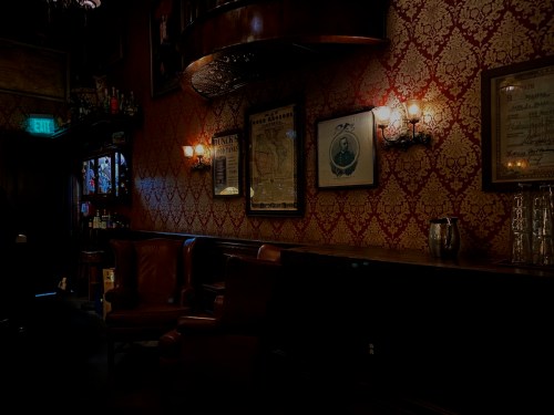 Cozy bar interior with vintage decor, leather chairs, ornate wallpaper, and dim lighting.