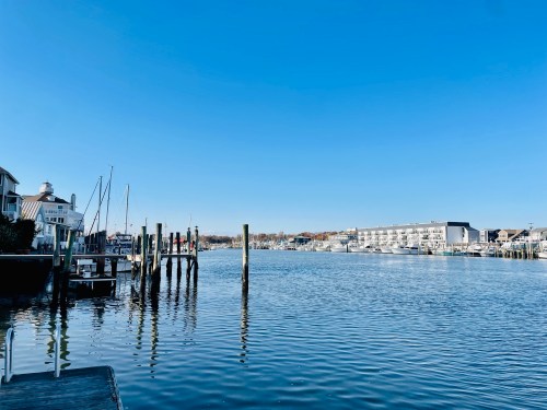 A calm waterfront scene with boats, docks, and clear blue skies reflecting on the water.