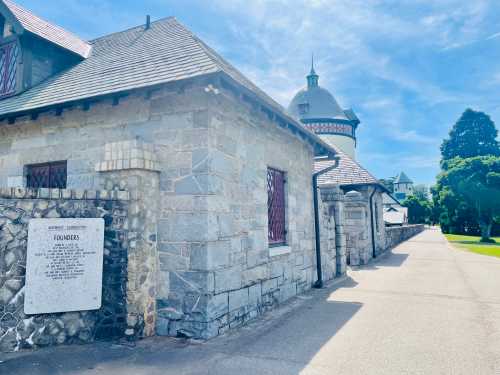 Stone building with a slate roof and a nearby tower, set against a clear blue sky and green trees.