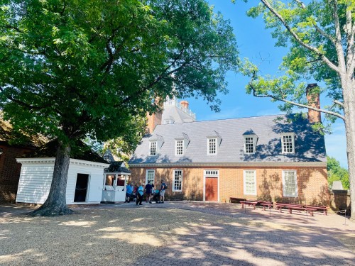 Historic brick building with a slate roof, surrounded by trees and a grassy area, with visitors approaching.