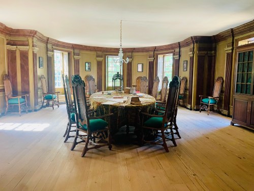 A spacious, elegantly furnished dining room with a large round table surrounded by ornate wooden chairs.