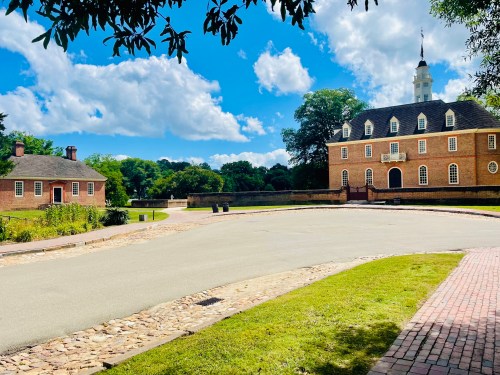A scenic view of a historic building and a smaller structure, surrounded by greenery and a blue sky with clouds.