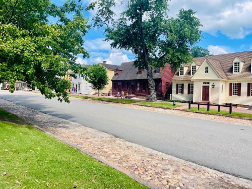 A quiet street lined with historic homes and trees under a blue sky with fluffy clouds.