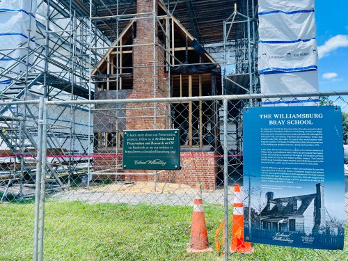 Construction site of the Williamsburg Bray School, featuring scaffolding and informational signs behind a fence.