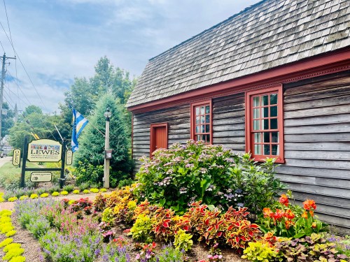 A charming wooden building with a shingled roof, surrounded by colorful flowers and a sign for Lewes.