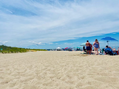 A sandy beach scene with people relaxing under umbrellas and enjoying the sunny day.