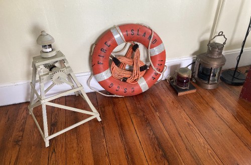 A vintage room with a life preserver labeled "Fire Island" and two lanterns on a wooden floor.