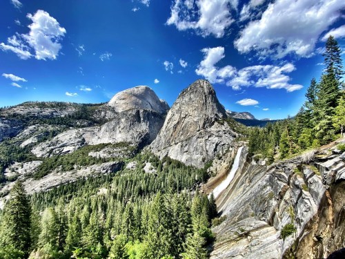 A panoramic view of granite mountains and lush green forests under a bright blue sky with scattered clouds.