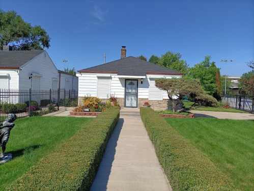 A well-maintained house with a manicured lawn, bordered by hedges and flower beds, featuring a decorative statue in the yard.