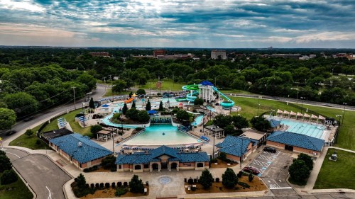 Aerial view of a water park featuring pools, slides, and green landscaping under a cloudy sky.