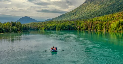 A raft filled with people floats down the Kenai River on a summer day in Alaska.