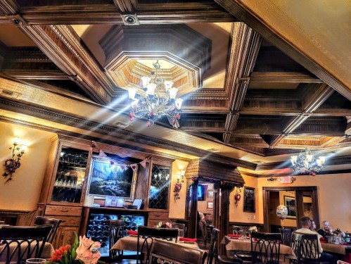 Elegant restaurant interior with wooden coffered ceiling, chandeliers, and cozy dining setup. Warm, inviting atmosphere.