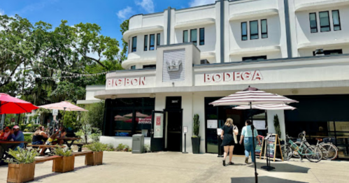 Exterior of Big Bon Bodega with outdoor seating, umbrellas, and bicycles parked outside on a sunny day.
