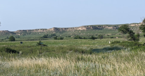 A scenic view of rolling green hills and a rocky cliff under a clear blue sky.