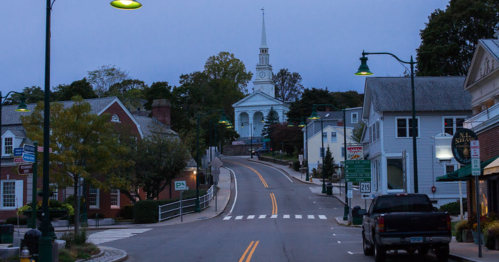 Quiet street scene at dusk, featuring a church steeple in the background and charming buildings lining the road.