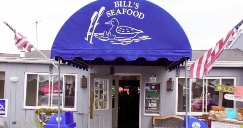 Exterior of Bill's Seafood restaurant with a blue awning featuring a duck logo and American flags at the entrance.