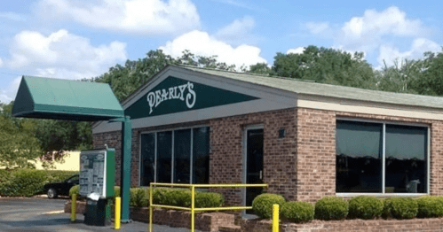 A brick restaurant building with large windows and a green awning, surrounded by shrubs and a clear blue sky.