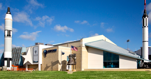 Exterior view of a space museum featuring rocket replicas, an American flag, and a clear blue sky.
