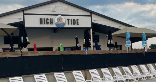 Exterior of a building labeled "High Tide," with colorful umbrellas and white lounge chairs in front.