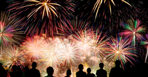 Silhouettes of people watching a vibrant fireworks display lighting up the night sky.